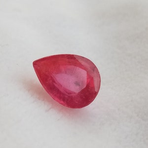 以下が含まれることがあります： 深い赤色の涙型のファセットカットのルビーの宝石です。