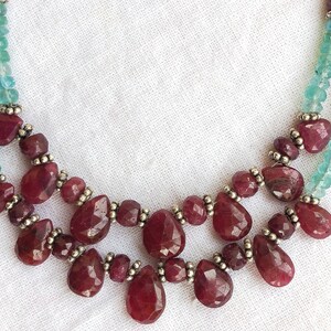 May include: A two-strand necklace with a silver chain and red gemstone beads. The necklace features a teardrop-shaped pendant with a cluster of red gemstones.