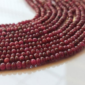 May include: A strand of deep red ruby beads, each bead is smooth and round, with a slight sheen. The beads are arranged in a loose, flowing pattern, creating a beautiful and elegant look.