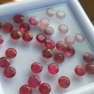 Puede incluir: Una colección de piedras preciosas rojas sueltas en una bandeja blanca. Las piedras preciosas son de varios tamaños y formas.