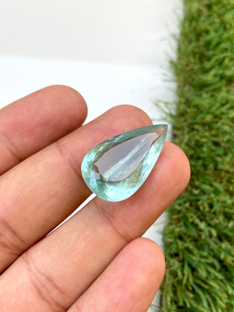 May include: A teardrop-shaped aquamarine gemstone with a light blue color.