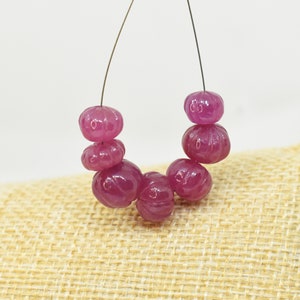 May include: A strand of pink carved gemstone beads. The beads are round and have a carved design. The beads are strung on a wire.
