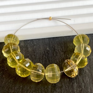 Może przedstawiać: Szereg fasetowanych, żółtych koralików z cytrynu nawleczonych na srebrny drut. Koraliki są okrągłe i mają polerowane wykończenie.