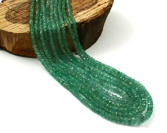 Pode incluir: Um fio de contas de pedras preciosas verdes, provavelmente esmeralda ou peridoto, com acabamento facetado. As contas são enfiadas em um fio transparente e estão dispostas em um padrão solto e fluido.
