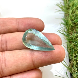 May include: A teardrop-shaped aquamarine gemstone with a light blue-green color. The gemstone is faceted and has a smooth, polished surface.