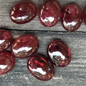 Puede incluir: Una colección de ocho piedras preciosas rojas ovaladas pulidas. Las piedras preciosas son lisas y brillantes, de un color rojo intenso.