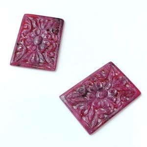 May include: Two carved pink ruby gemstones with a floral design. The gemstones are rectangular in shape and have a polished finish.