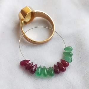 May include: A strand of emerald green and ruby red gemstone beads strung on a silver wire. The beads are teardrop shaped and are arranged in an alternating pattern.