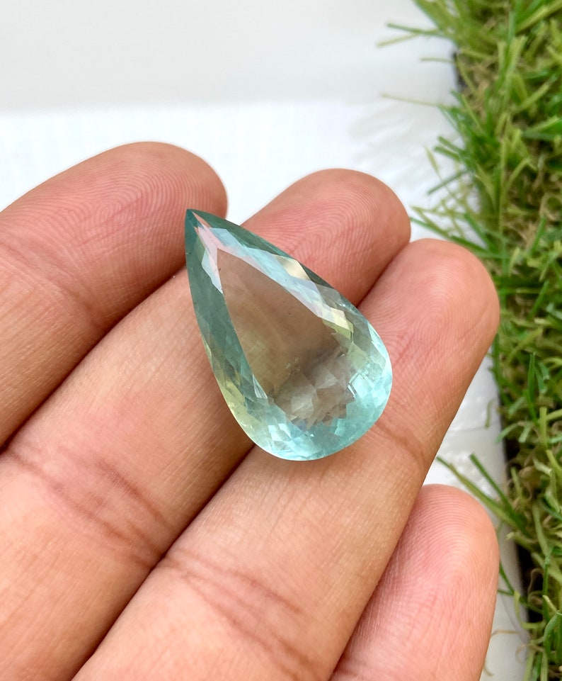 May include: A teardrop-shaped aquamarine gemstone with a light blue and green color.