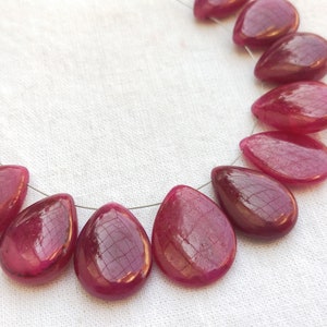 Puede incluir: Una hebra de cuentas de piedras preciosas de color rojo intenso en forma de lágrima. Las cuentas están enhebradas en un alambre de plata.