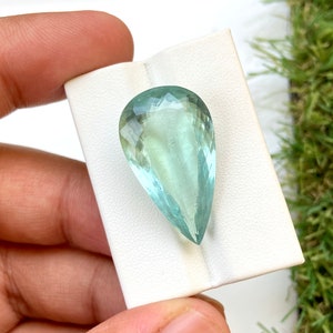 May include: A pear-shaped aquamarine gemstone with a light blue color. The gemstone is faceted and has a smooth, polished finish.