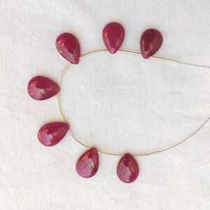 May include: Seven teardrop-shaped gemstone beads strung on a silver wire. The beads are a deep, rich red color.