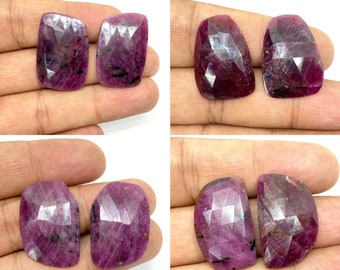 Può includere: Quattro pietre preziose di rubino rosa sfaccettate, ciascuna con un taglio e una forma unici, sono esposte su una mano. Le pietre preziose sono di un colore rosa intenso con una leggera sfumatura viola.