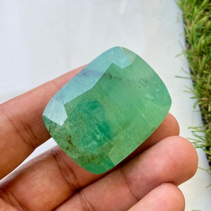 May include: A large, green, faceted gemstone with a rectangular shape. The gemstone has a light green color and is translucent.