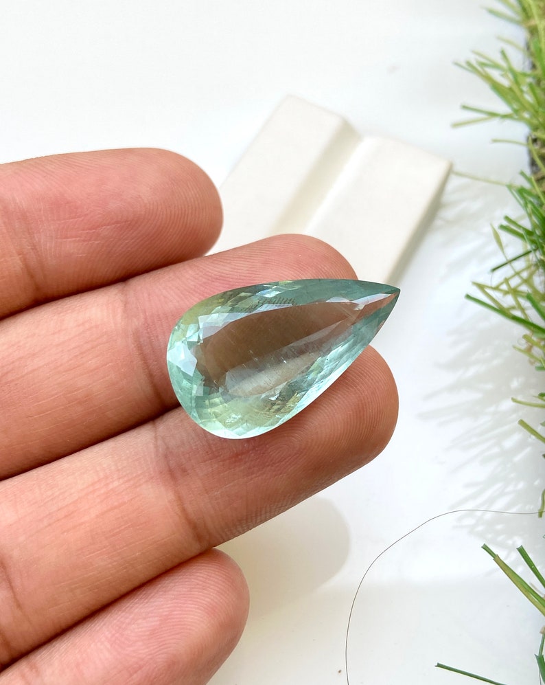 May include: A teardrop-shaped aquamarine gemstone with a light green hue.