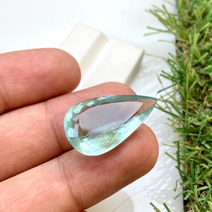 May include: A teardrop-shaped aquamarine gemstone with a light blue color. The gemstone is faceted and has a high degree of clarity.