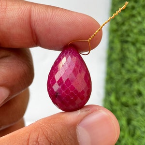 May include: A deep red faceted gemstone pendant with a gold wire loop.