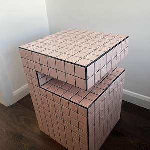 May include: A pink and black tiled side table with a unique design. The table has a square top and a square base with a cutout in the middle.