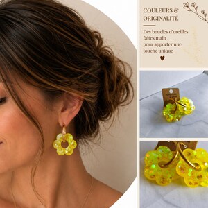 May include: A pair of bright yellow flower-shaped earrings featuring a translucent resin material with embedded glitter particles. The floral charms are suspended from simple gold-toned metal hoops. The earrings are displayed on a brown card.