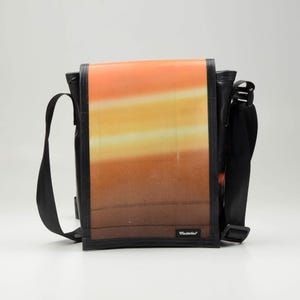 Peut inclure: Un sac à bandoulière noir avec une bandoulière réglable. Le sac présente un design ombré coloré avec des nuances d'orange, de jaune et de brun. Le sac a une petite étiquette noire avec le texte "Mustache" dessus.