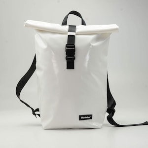 Puede incluir: Mochila blanca con cierre enrollable, correas y hebilla negras. La bolsa tiene un acabado brillante y una pequeña etiqueta negra con texto blanco en la parte inferior. Con asa superior y correas ajustables.
