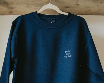 Op de afbeelding: Een donkerblauw sweatshirt met de tekst "cute but psycho" geborduurd op de voorkant.