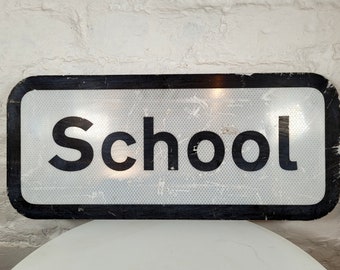 May include: A black and white reflective sign with the word "School" in large black letters.