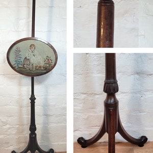 May include: A dark wood fire screen with a needlepoint panel depicting a girl with a lamb. The screen has a tripod base with a carved finial.