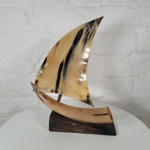 May include: A decorative sailboat sculpture made from horn with a dark wood base. The sail is a light brown color with dark brown stripes.