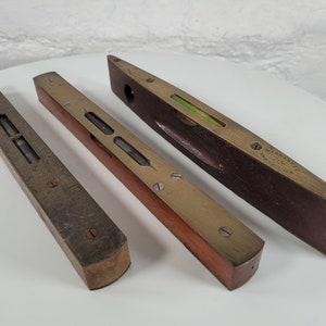 Puede incluir: Cuatro niveles de madera vintage con incrustaciones de latón. Los niveles tienen una burbuja verde y están marcados con "Warrington & Jim Ltd. Made in England."