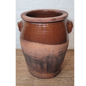 Op de afbeelding: Een grote, bruine keramische pot met twee handvatten. De pot heeft een brede opening en een licht afgeronde bodem. De pot is geglazuurd in een bruine kleur met een donkerdere bruine glazuur op de bodem.