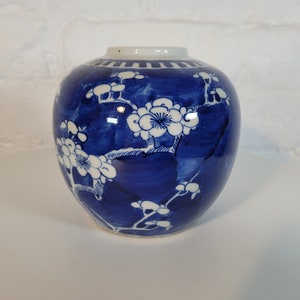 May include: A small blue and white porcelain jar with a floral design. The jar has a round body and a narrow neck. The floral design is in white and features branches with delicate flowers.