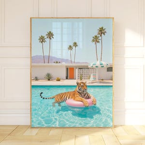 Peut inclure: Impression d'art encadrée représentant un tigre se prélassant sur un anneau gonflable rose dans une piscine turquoise. Des palmiers, une maison moderne du milieu du siècle et un ciel bleu créent une ambiance tropicale rétro. L'œuvre est dans un cadre en bois.