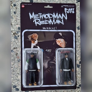 Puede incluir: Set de figuras de acción con Method Man y Redman, titulado "Blackout!". El embalaje es negro con texto blanco, incluyendo "B-ART TOYS". Las figuras están en estuches de plástico transparente, una con un atuendo verde y negro y la otra con un traje negro.