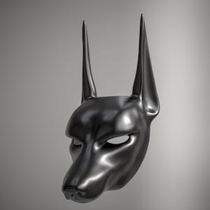 Può includere: Una maschera nera a forma di testa di cane, con orecchie a punta e una superficie liscia e riflettente. La maschera presenta aperture per gli occhi e un muso dettagliato.