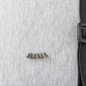 Pu&ograve; includere: Primo piano di cinque piccole viti color bronzo disposte in linea orizzontale. Sono su un tessuto grigio chiaro strutturato. Un cinturino nero con fibbia &egrave; visibile in basso e a destra.
