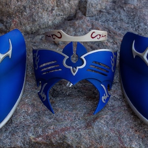 May include: A set of blue and silver cosplay armor pieces, including two shoulder guards, a headpiece, and a forehead band. The armor has a metallic silver trim and accents, with a matte blue finish.