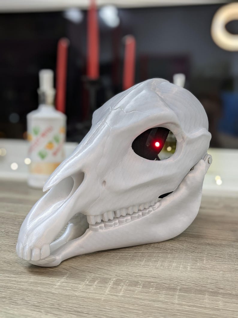 May include: A white 3D printed animal skull mask with a red light in the eye socket.