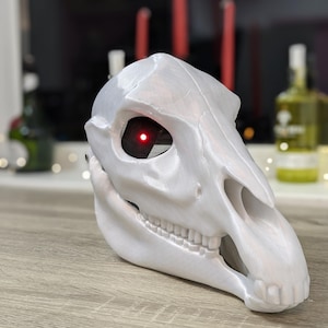 May include: White horse skull mask with a red glowing eye. The mask is made of a smooth, white material and has a detailed design.