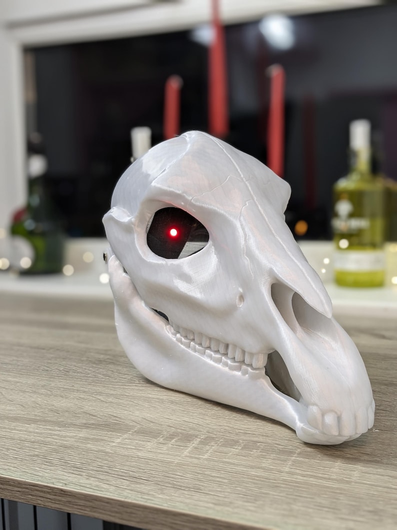 May include: White horse skull mask with a red glowing eye. The mask is made of a smooth, white material and has a detailed design.