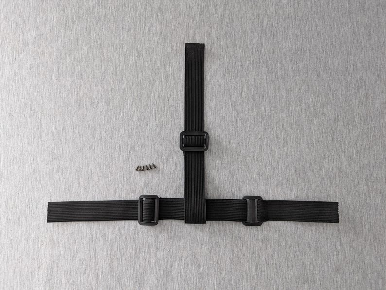 Pu&ograve; includere: Assemblaggio di cinghie elastiche nere con tre fibbie e un piccolo mucchio di viti. Le cinghie sono disposte a forma di T su uno sfondo grigio. Le fibbie sono quadrate e in plastica nera.