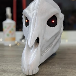 May include: White 3D printed animal skull mask with red glowing eyes. The mask has a long snout and detailed teeth.