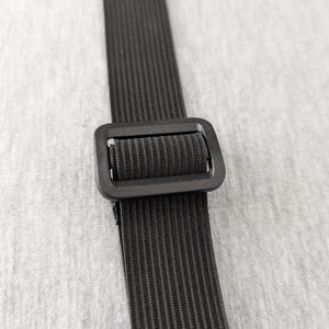 Pu&ograve; includere: Primo piano di un cinturino nero a coste con fibbia rettangolare. Il cinturino &egrave; realizzato in un materiale resistente e strutturato. Lo sfondo &egrave; un tessuto grigio chiaro.