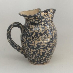 May include: A ceramic pitcher with a speckled blue and cream glaze. The pitcher has a wide mouth and a handle.