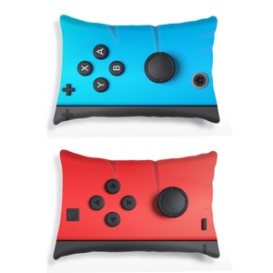 May include: Two decorative pillows shaped like a video game controller. One pillow is blue with black buttons and the other is red with black buttons.