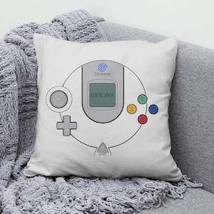 May include: White pillow with a gray and white illustration of a Sega Dreamcast controller. The controller has the text "Dreamcast" and "RELAX" on it.
