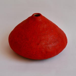 May include: A bright red ceramic vase with a rounded, conical form. The vase features a small opening at the top and a textured surface. The design is simple and modern, suitable for home decor, with a height of approximately 15 cm.