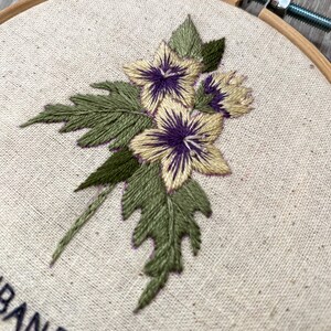 May include: Embroidered hoop art featuring a bouquet of three yellow flowers with purple centers and green leaves.