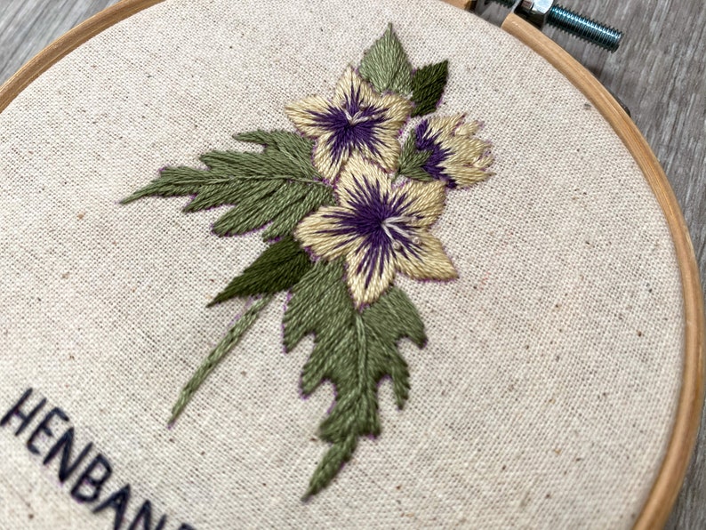 May include: Embroidered hoop art featuring a bouquet of three yellow flowers with purple centers and green leaves.