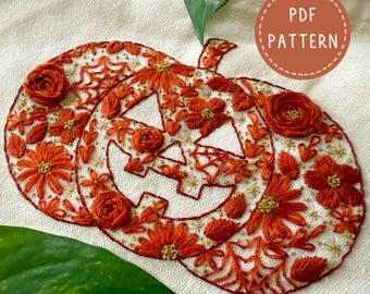Puede incluir: Diseño de calabaza bordada con detalles florales naranjas y una cara tallada. La calabaza está llena de flores naranjas, hojas y detalles dorados. El texto "PDF PATTERN" está en un círculo en la esquina superior derecha. El diseño está sobre una tela color crema.
